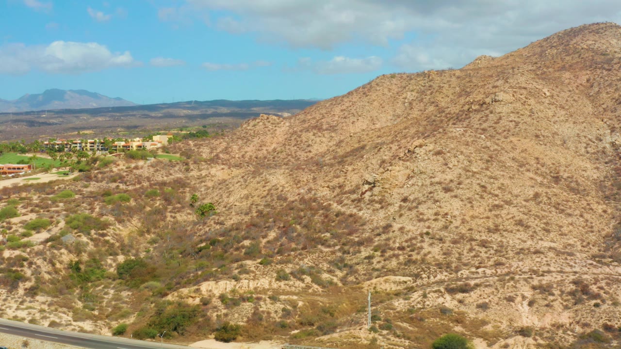 Arid hillside and valley with distant buildings under a blue sky.