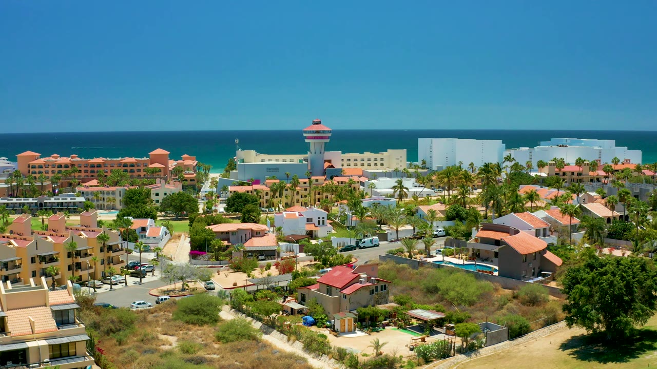 San Jose Del Cabo aerial view with more of the right-side neighborhood visible, including orange-roof homes, swimming pools, parked cars, oceanfront buildings, blue water, and no visible people.