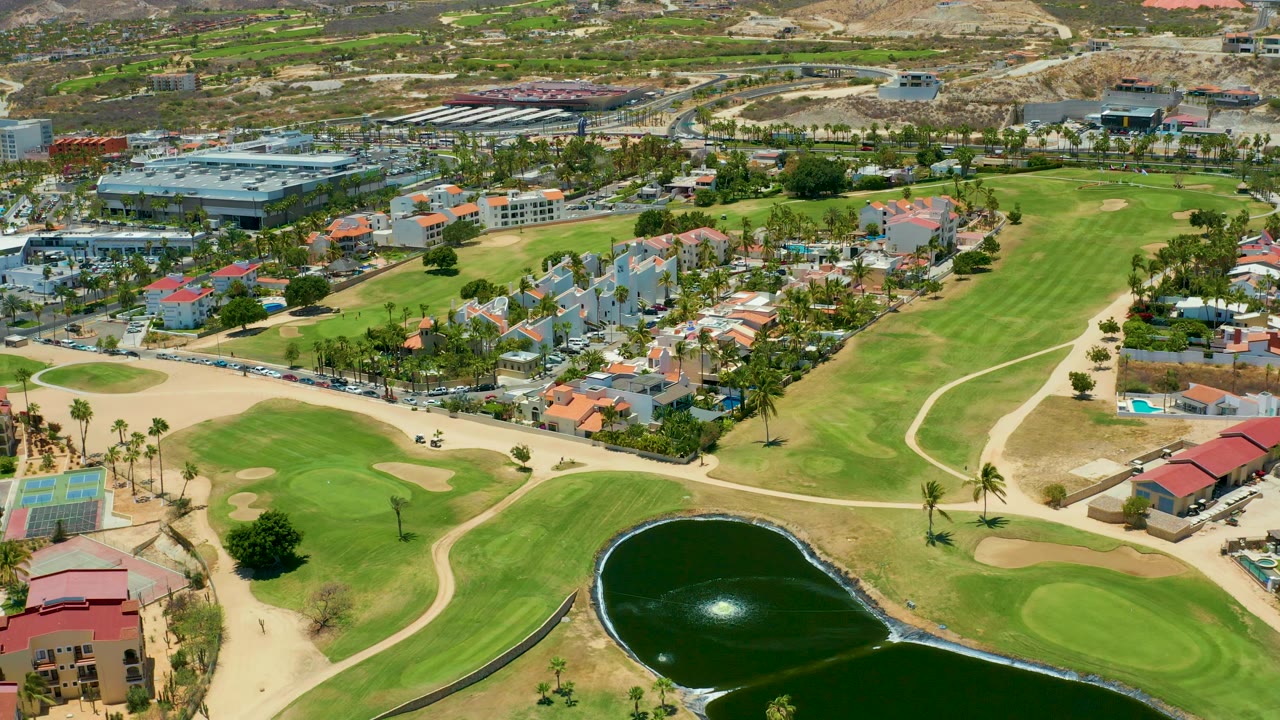 Aerial view across golf greens, pond, residential homes, roads, and hills.