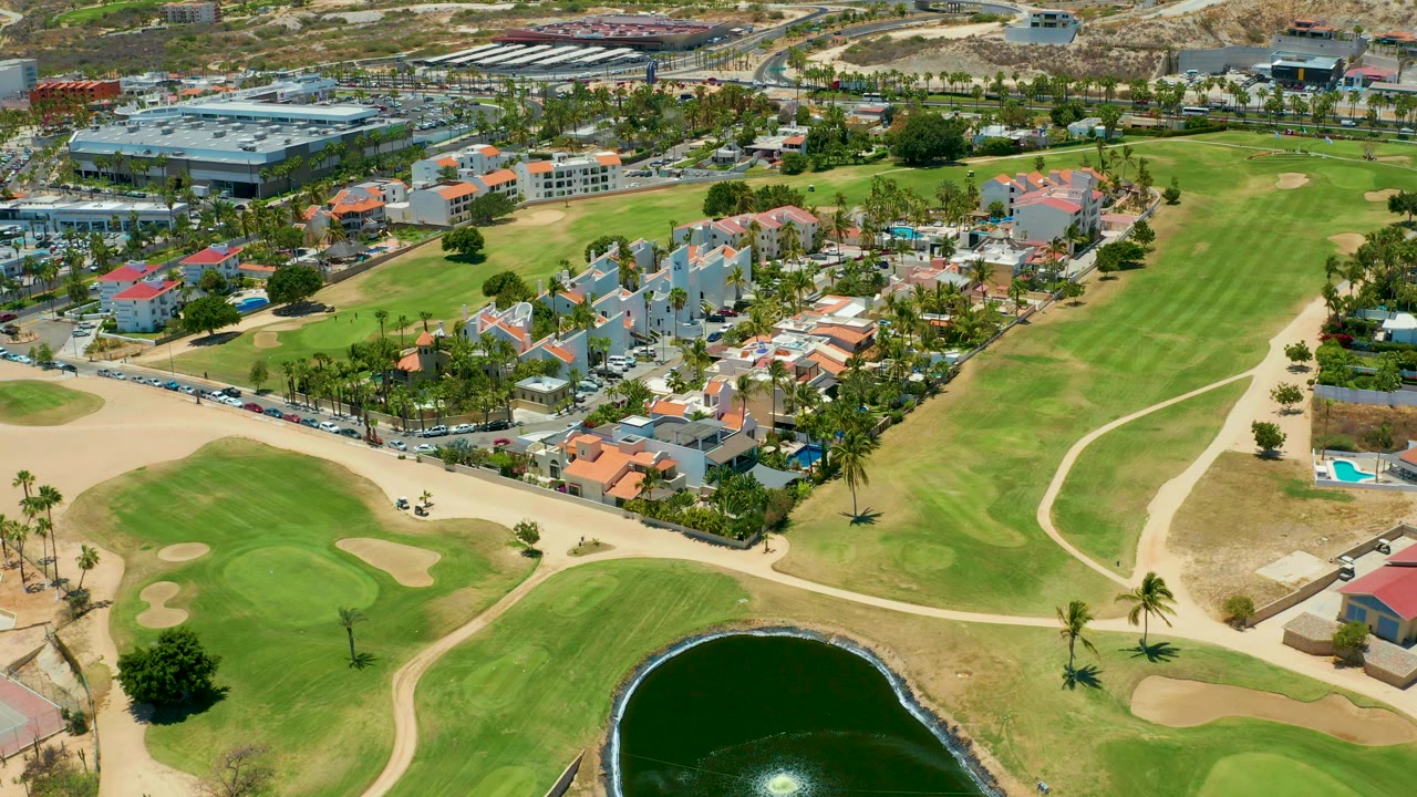 Elevated view across fairways, a pond, palm trees, roads, and clustered homes.