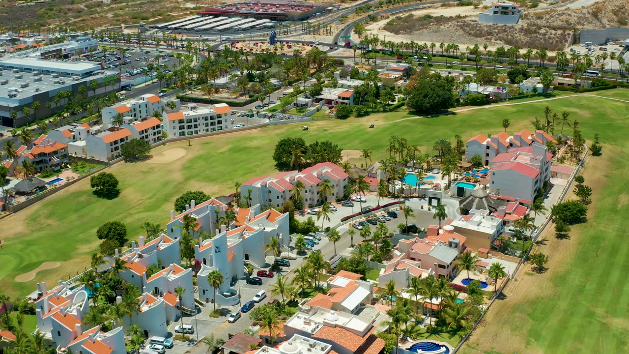 Aerial angle over homes, palm trees, pools, and golf course grass.