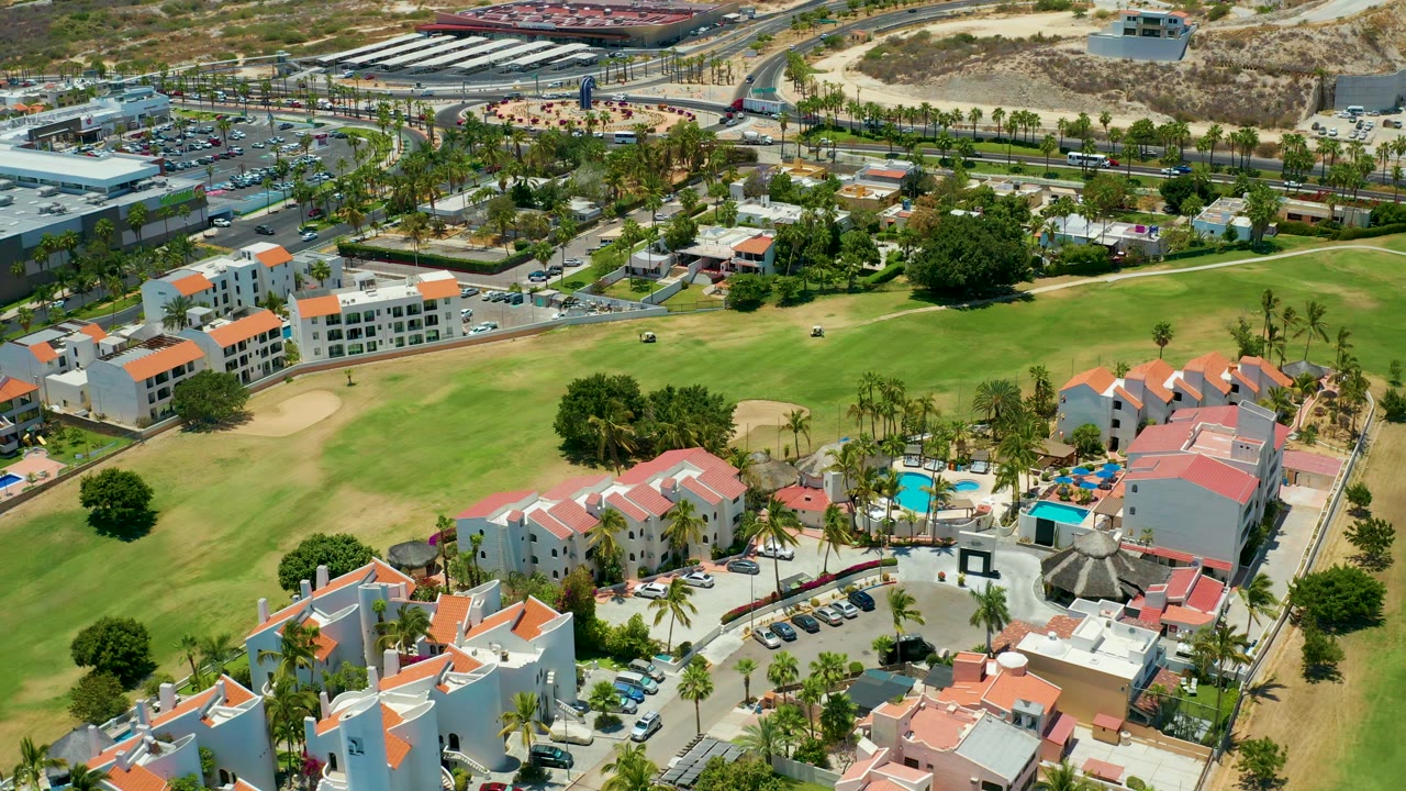 Aerial resort complex with red-roofed buildings beside a green golf course.