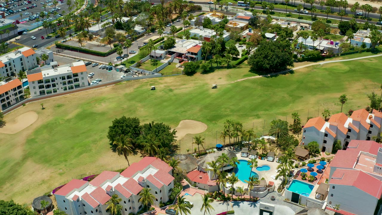 High angle view of fairway, sand trap, resort buildings, road, and parked cars.