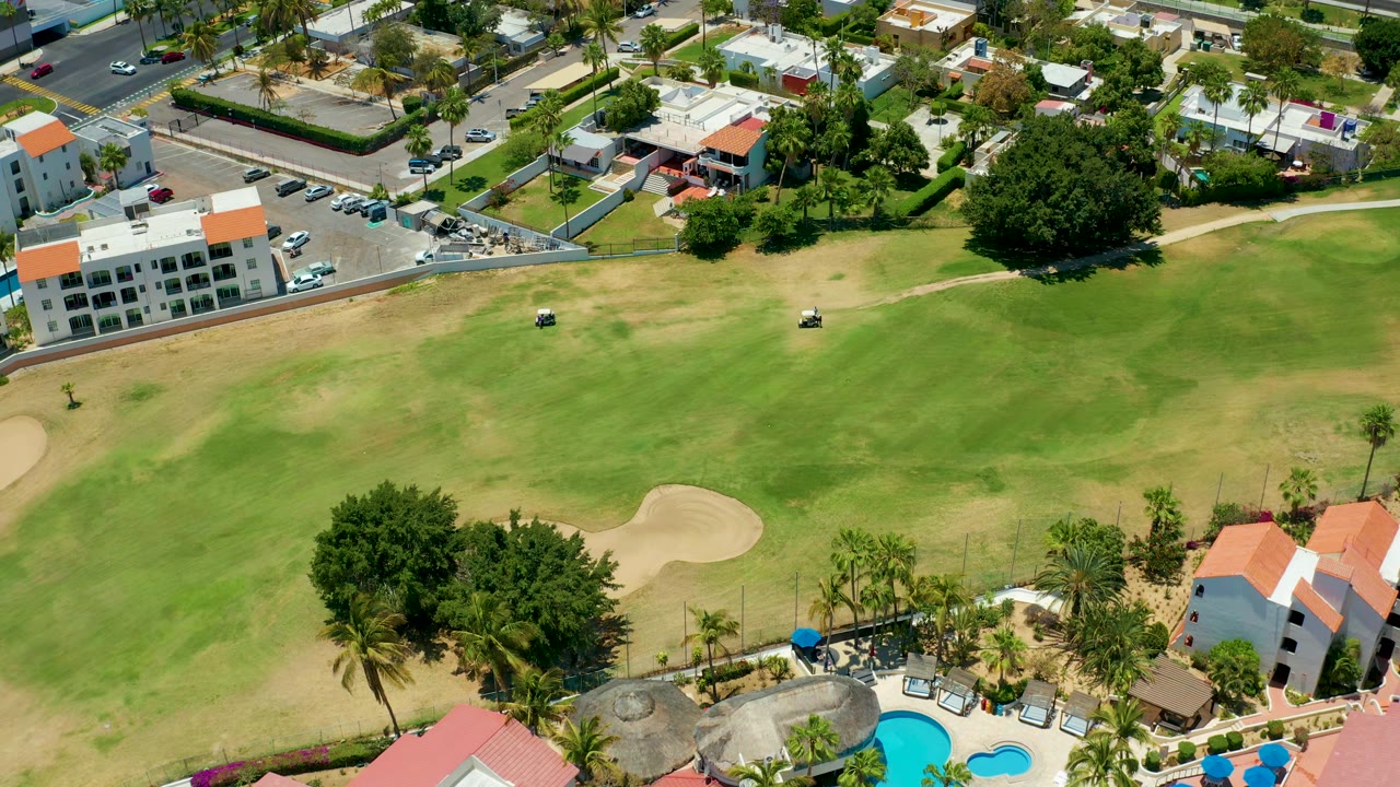 Aerial golf course view with two small carts on grass, buildings, trees, and a pool edge.