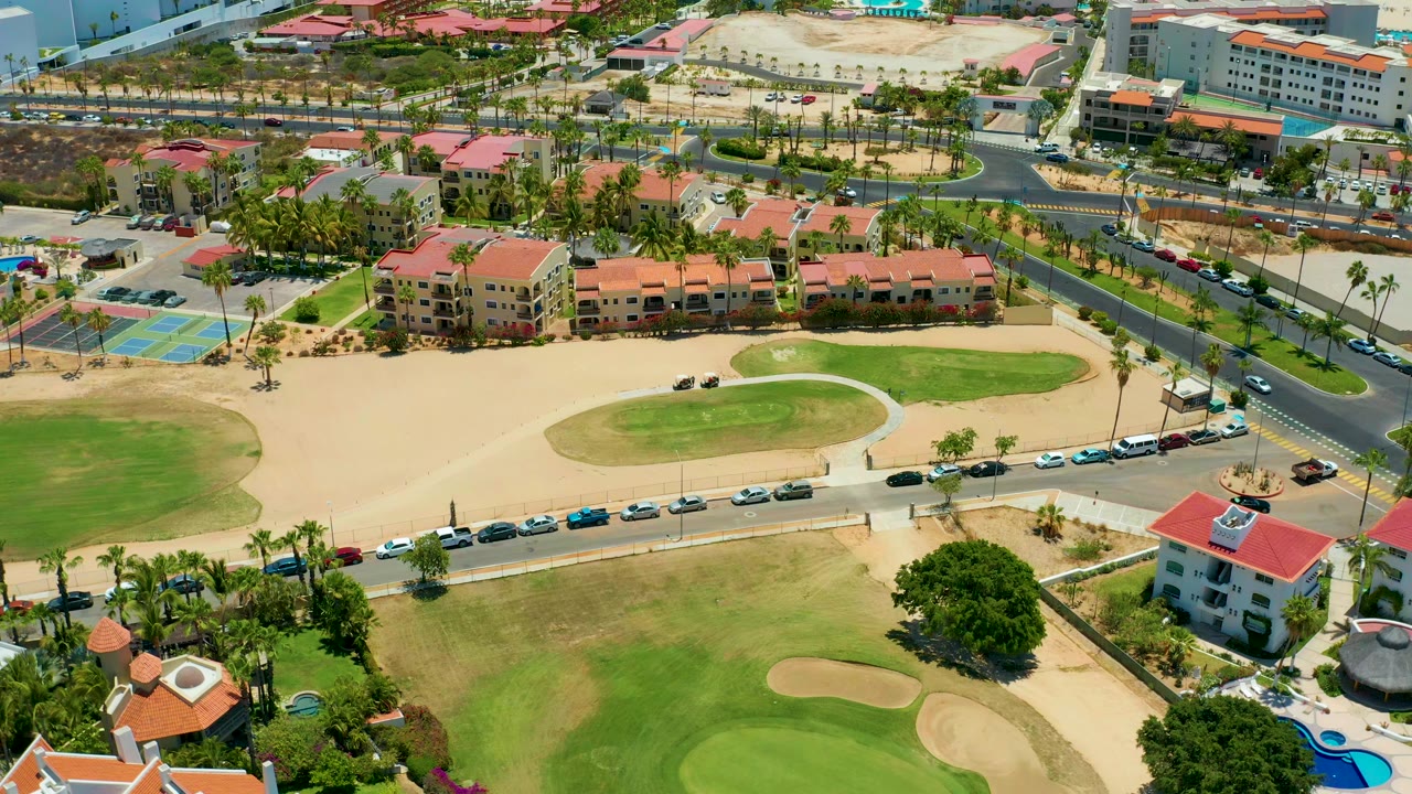 Overhead golf course view with cars along the road and residential buildings beyond.
