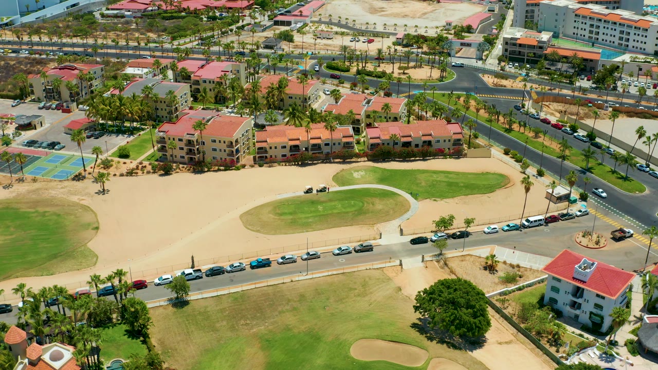 Overhead view of golf course edge, road traffic, palms, and residential buildings.