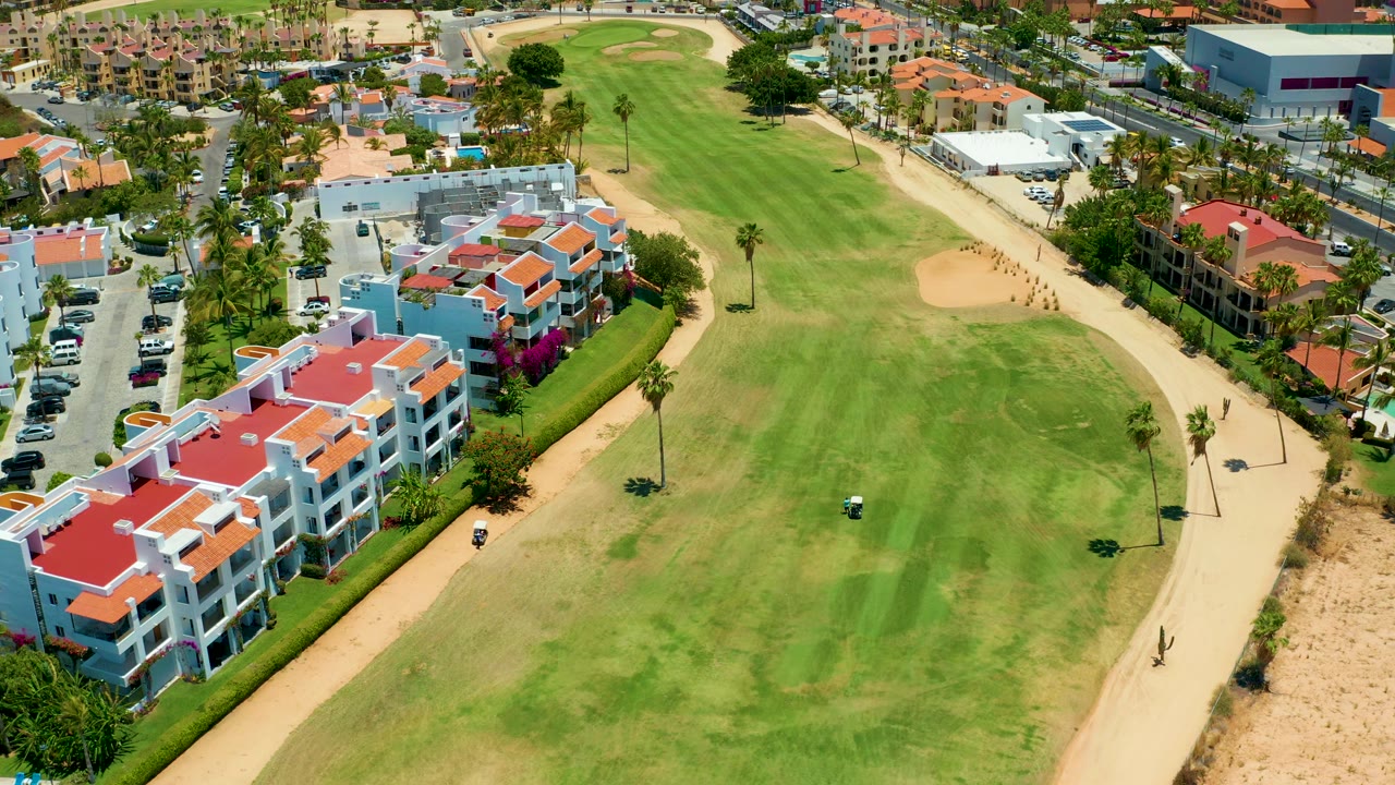Golf course aerial with residential blocks, palms, and a fairway bunker.