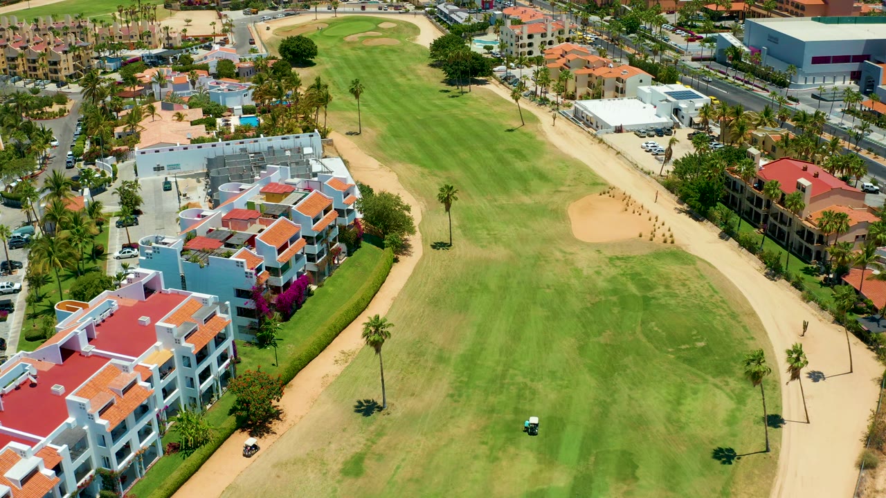 Aerial golf course with cart paths, palms, and urban buildings