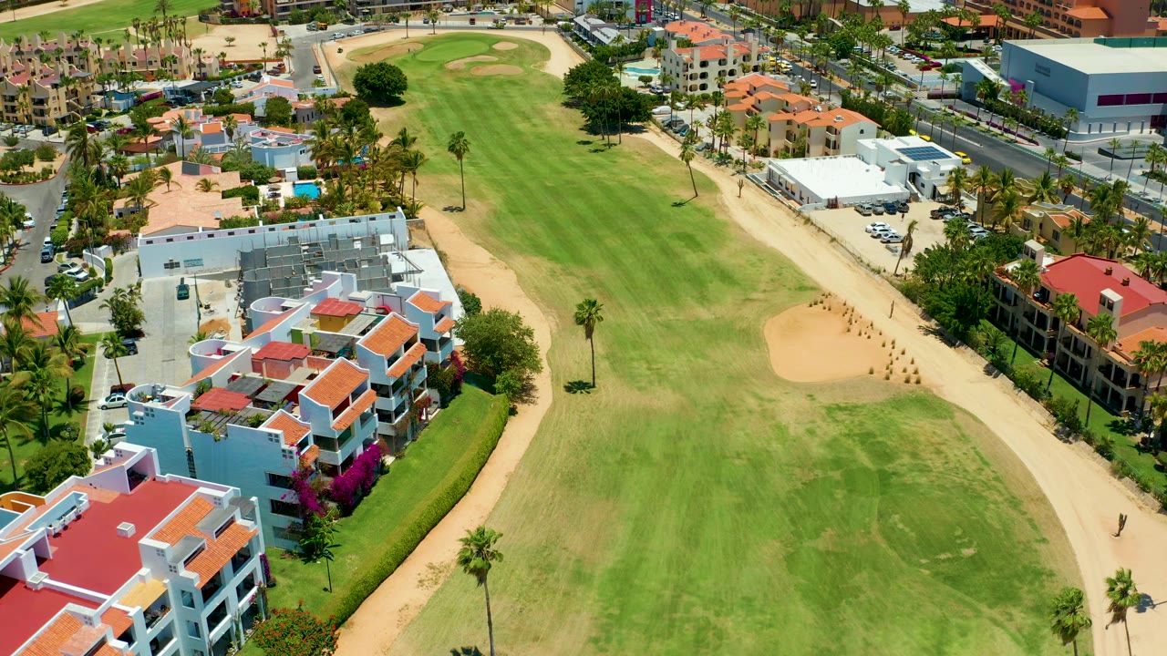 Overhead golf course view with sand bunker, white tent, cars, and nearby homes.