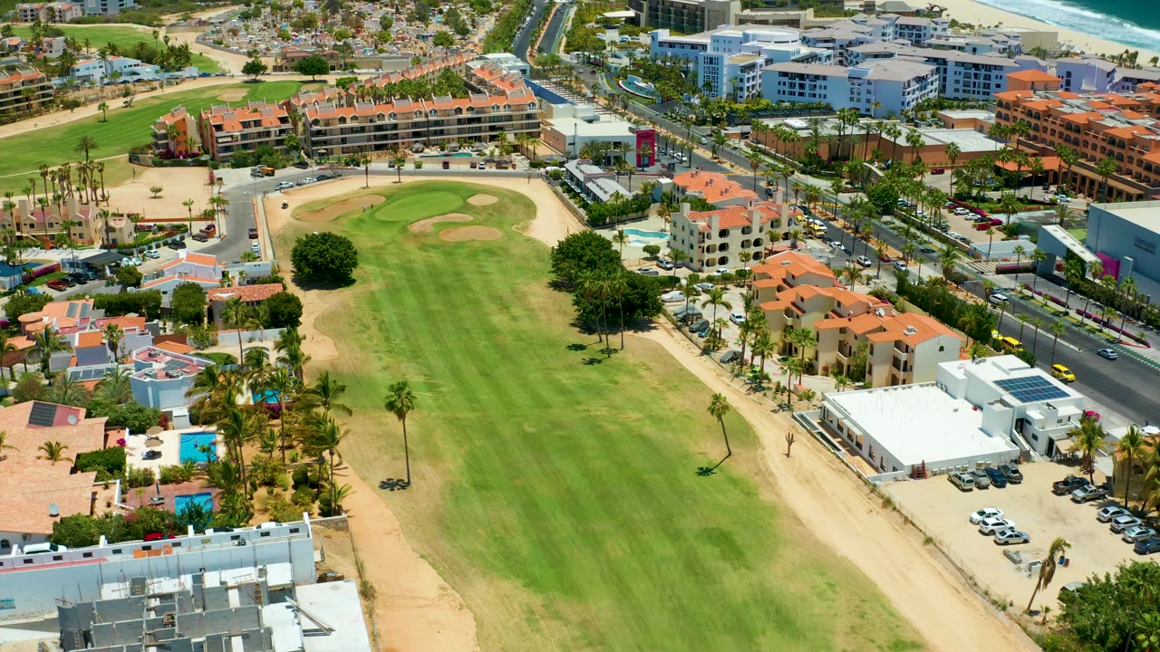 Aerial fairway view with sandy border, palms, buildings, and cars