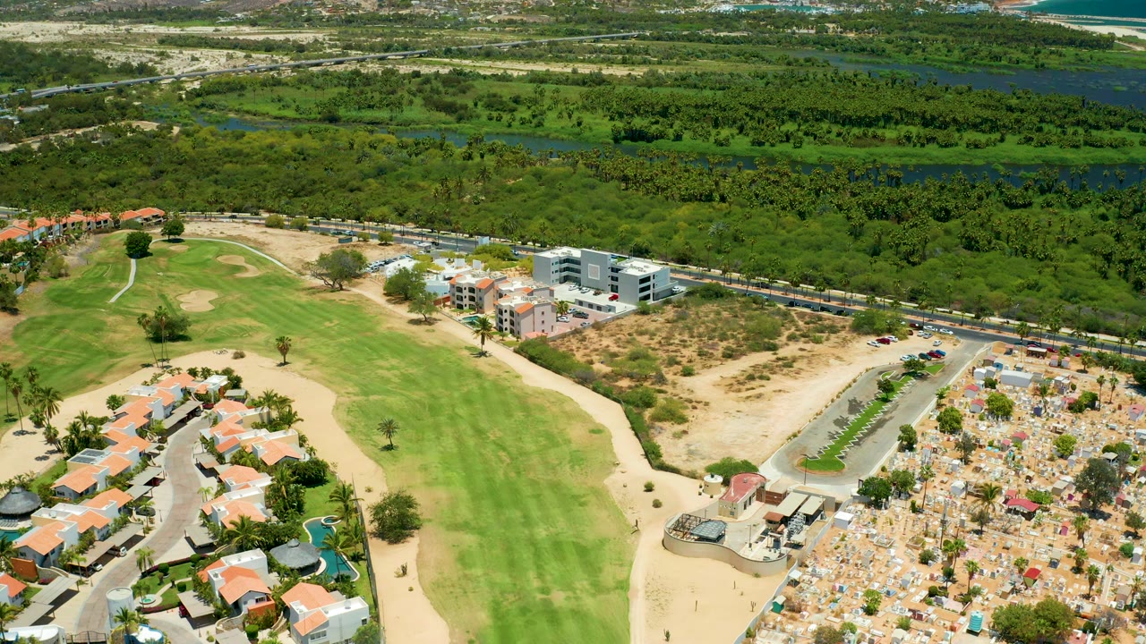 Drone view over a golf fairway beside homes, road, dry lots, trees, and waterway.