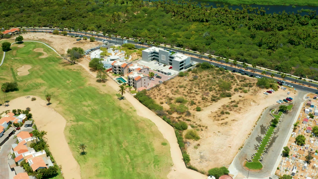 Aerial frame of fairway, dry lot, roadside vehicles, and residential area.