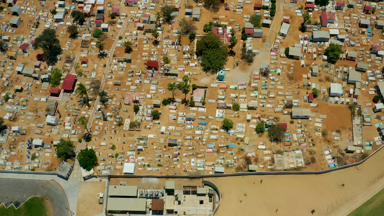 High overhead frame from San Jose Del Cabo, Baja California Sur, showing sandy lots, clustered small buildings, scattered trees, and pale paths running through the dense area, with no visible people.