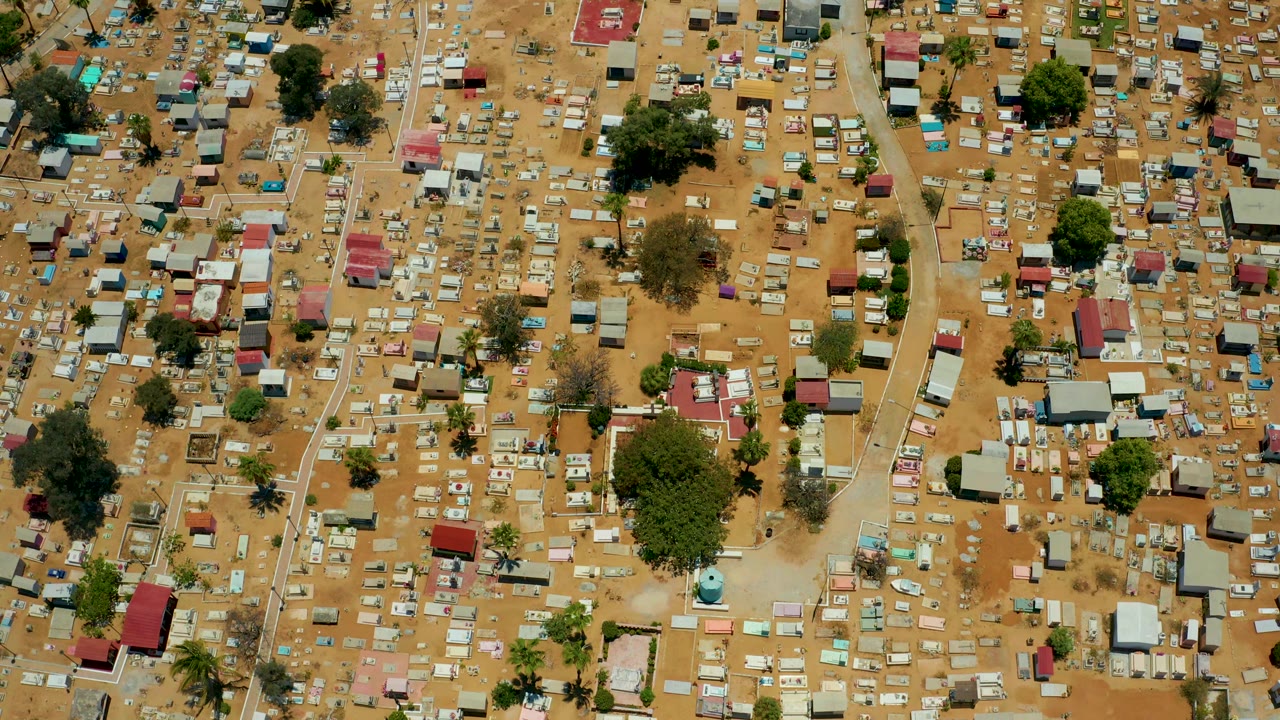 Dense overhead settlement with pale dirt lanes, small roofs, and scattered green trees.