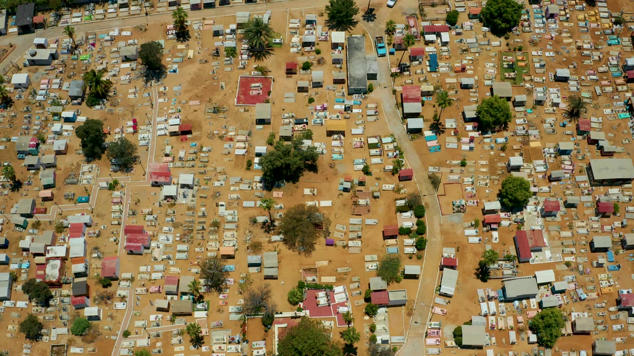 Overhead San Jose Del Cabo frame showing tan ground filled with small colorful roofed structures, larger shade trees, footpaths, and no visible people.