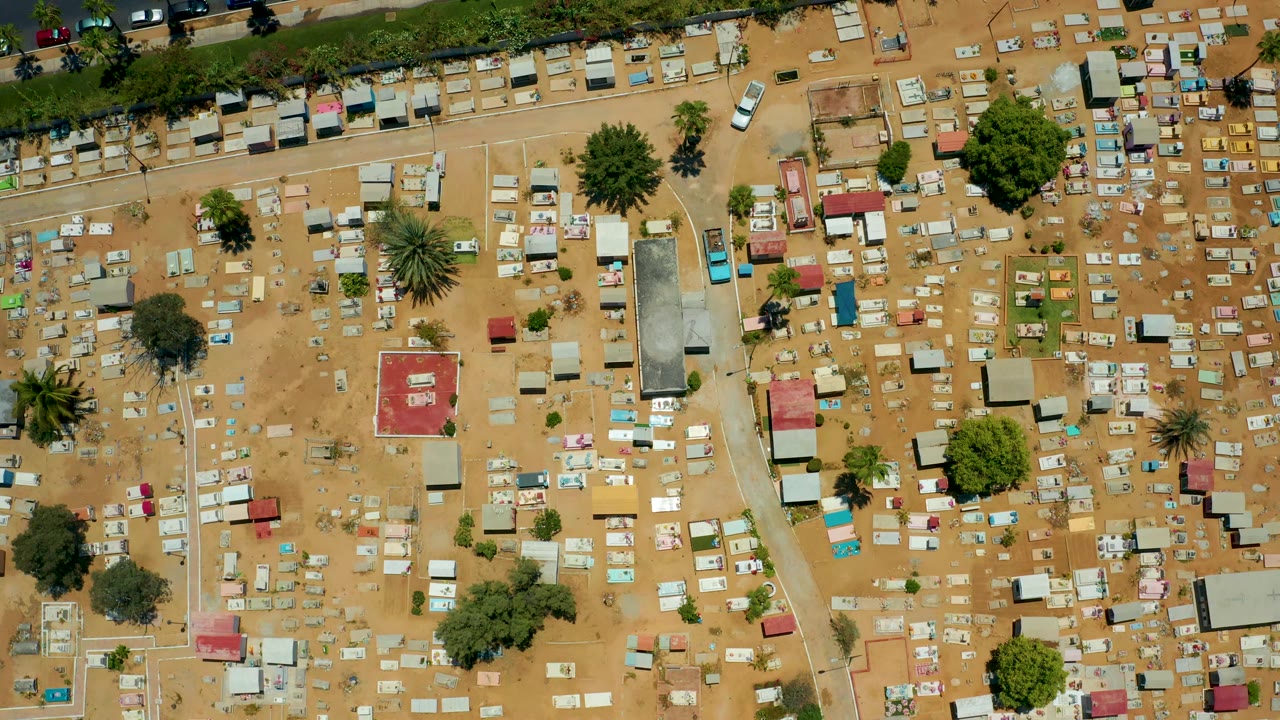 Overhead cemetery with a red-roofed structure, scattered grave markers, trees, and road above.