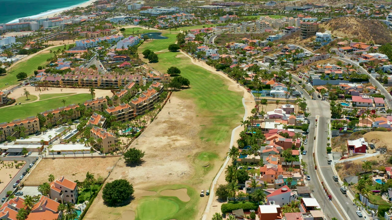Drone view of golf fairways, coastal homes, road traffic, and blue ocean