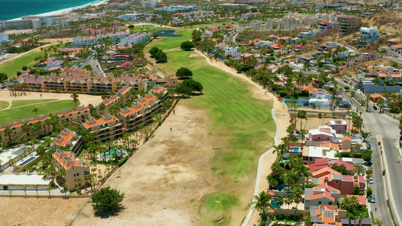 Aerial view of coastal residences beside dry grass and a green fairway.