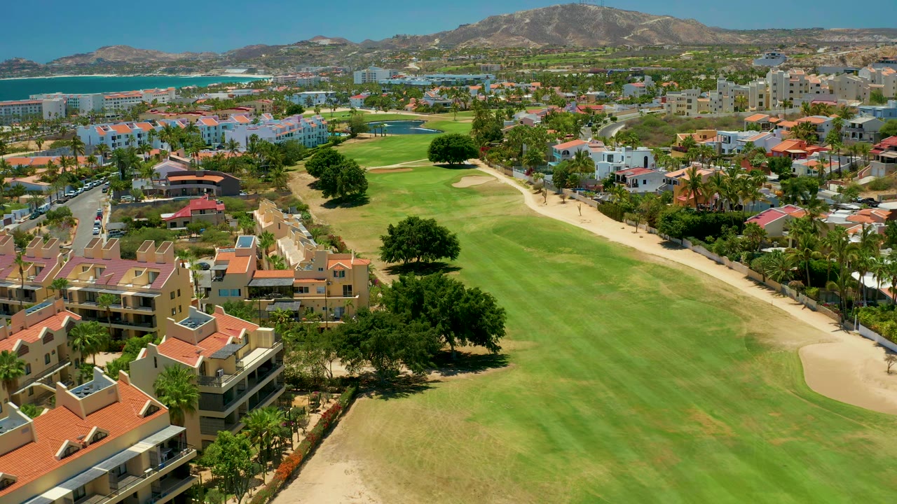 Drone view of a golf fairway bordered by homes and trees.