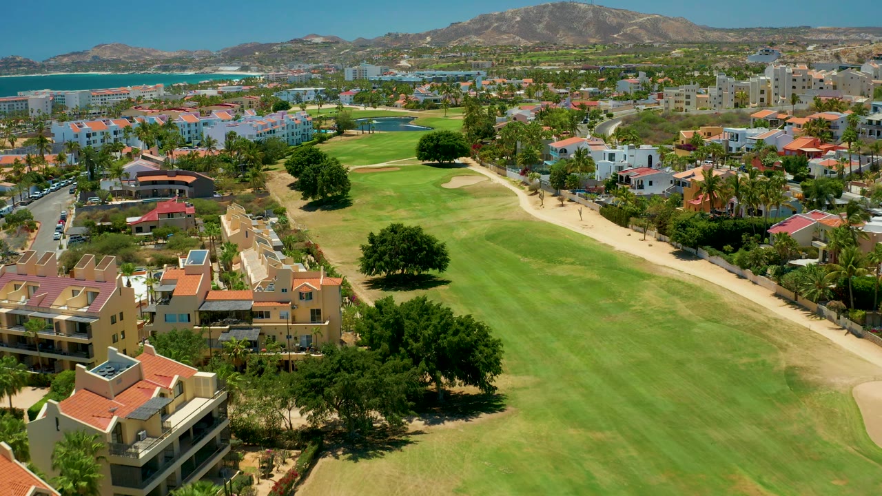 Aerial pass over a fairway with apartment buildings and ocean beyond.