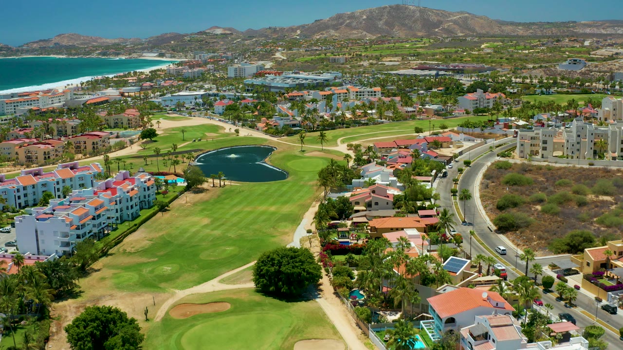 Wide aerial over golf course, pond, residences, ocean, and hills.