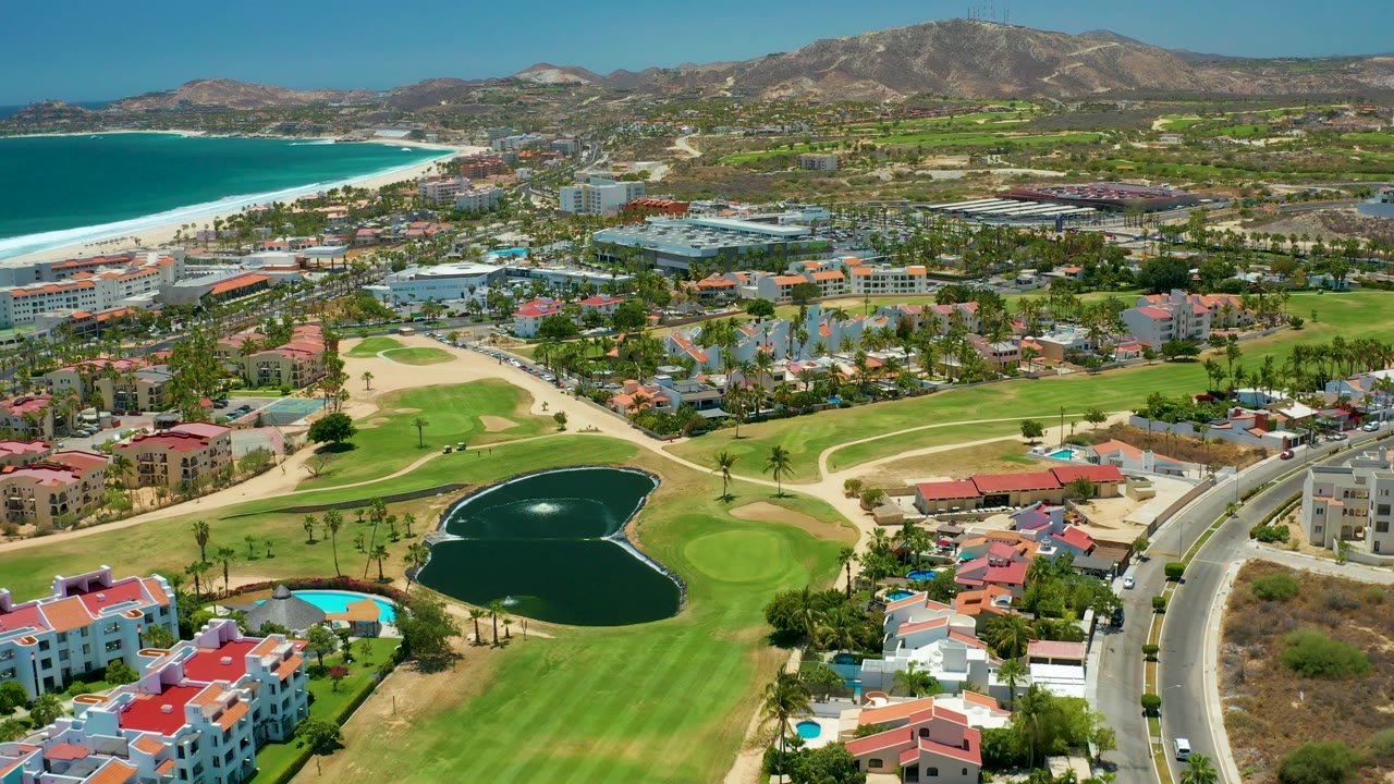 Golf course, dark pond, ocean beach, buildings, roads, and mountains seen from above.
