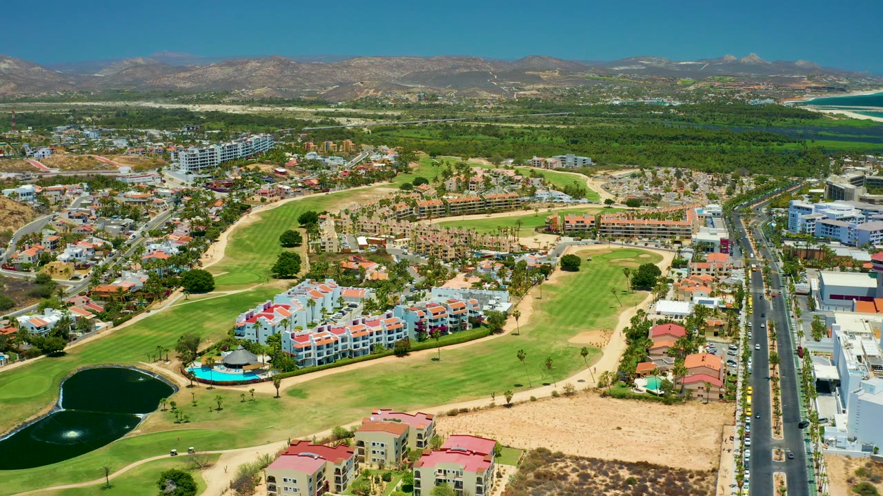 Residential area and golf course seen from above with road traffic and mountains.