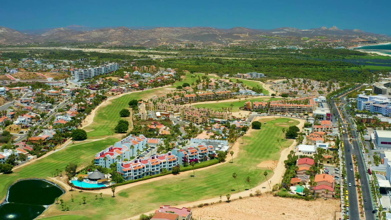 Drone view of residential buildings beside a green golf course and main road.