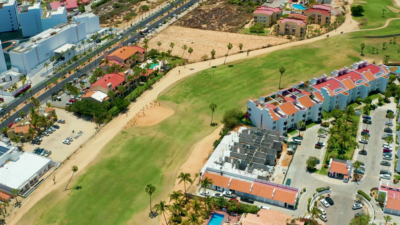 Aerial view across fairway grass, sand trap, roads, and low-rise buildings.
