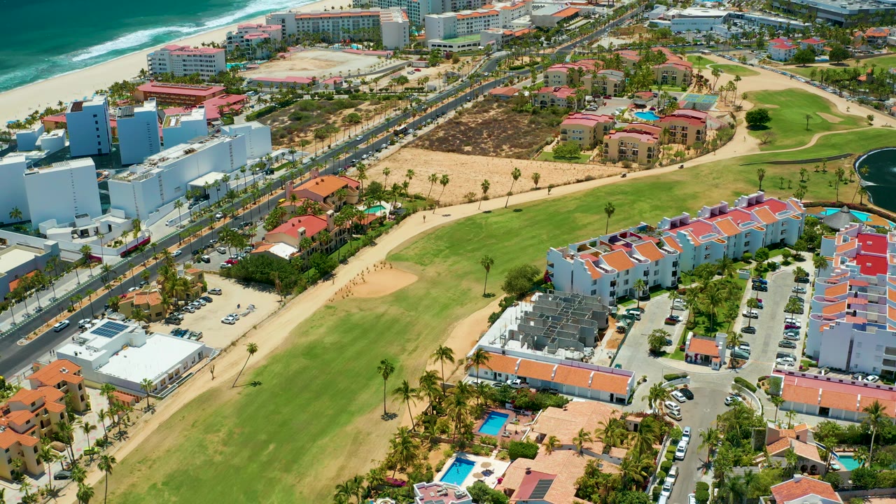 Aerial coast scene with ocean, road traffic, golf course, and buildings.