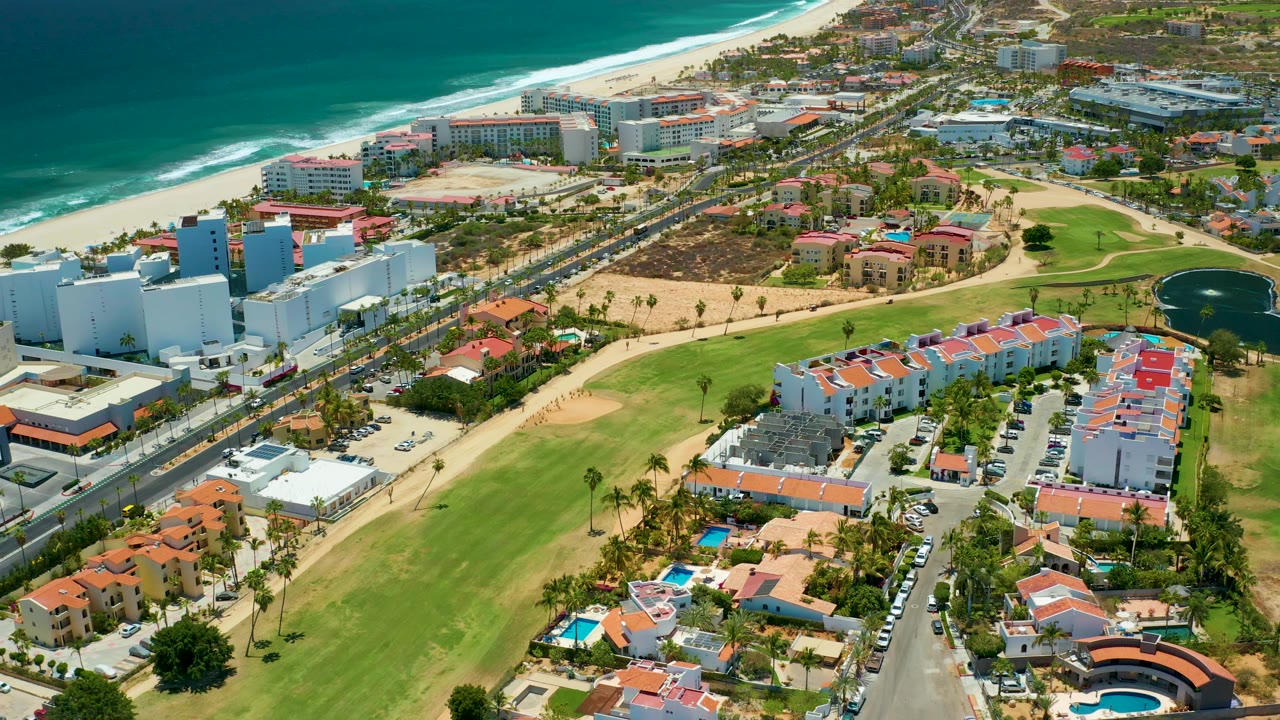 Coastal residential area with beach, road, lawns, and white buildings.