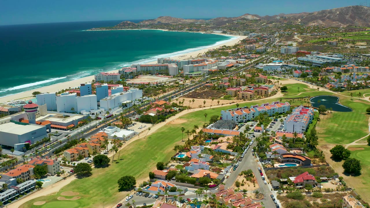 Wide aerial view of beachside highway, golf course, homes, and ocean.