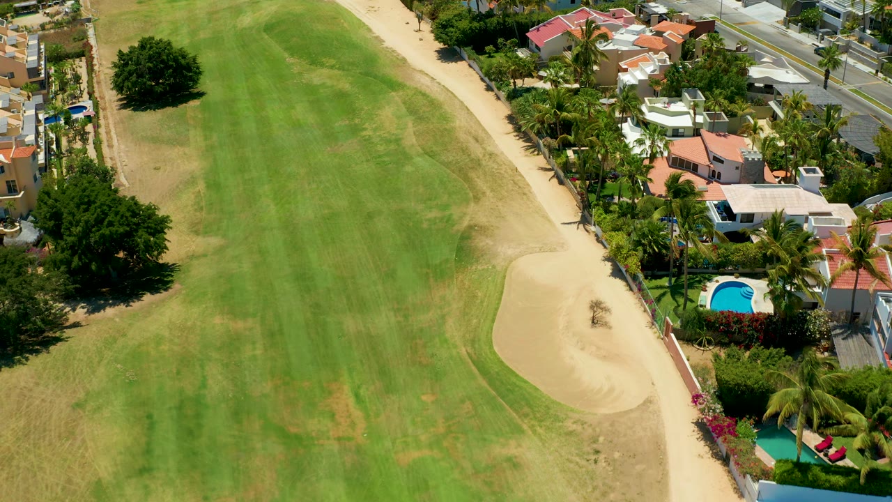 Aerial frame of golf fairway and sand bunker next to residential homes and palms.