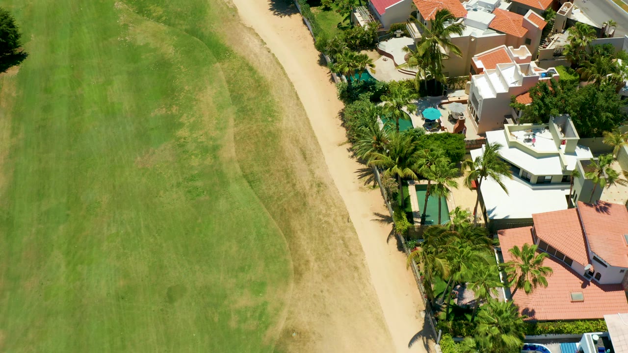 Aerial view of a sandy path between a field and red-roofed homes.