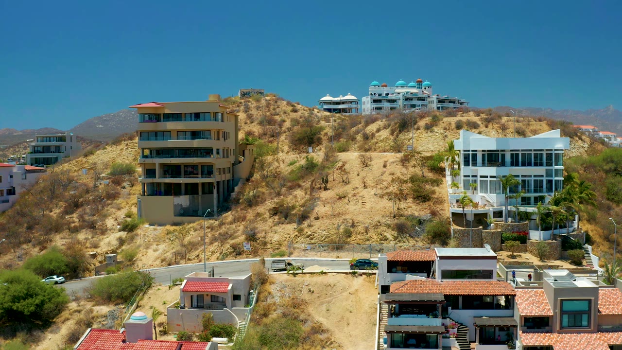 Hillside residences with balconies, red roofs, and sparse vegetation.