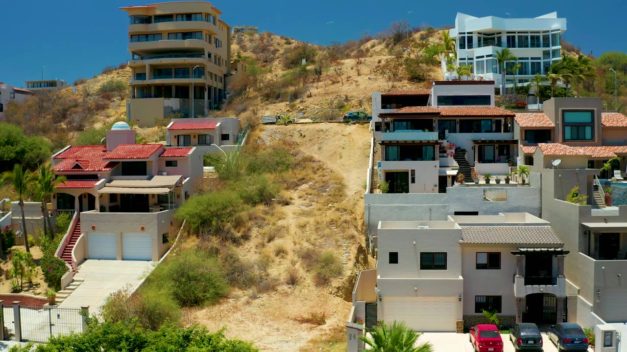 Modern hillside houses and dry slope under clear sky.