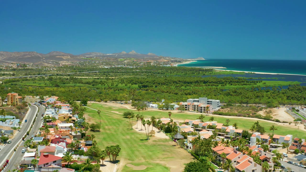 Coastal aerial with road, homes, golf course, buildings, mountains, and ocean