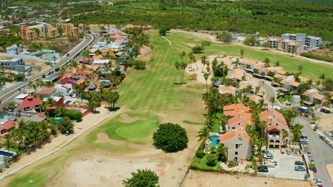Aerial pass over fairways, houses, and a roadside neighborhood.