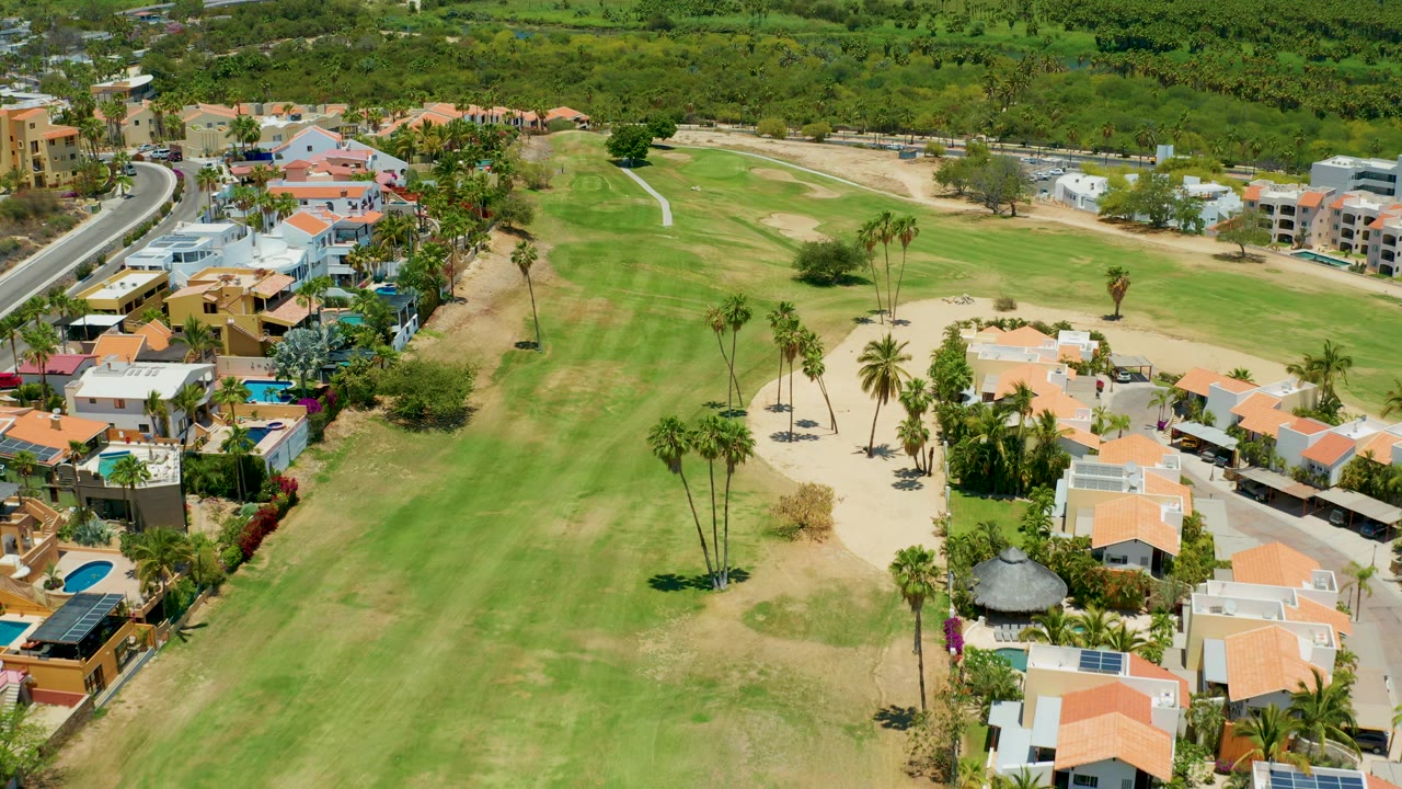 Drone view of a fairway bordered by orange-roofed houses and palms.