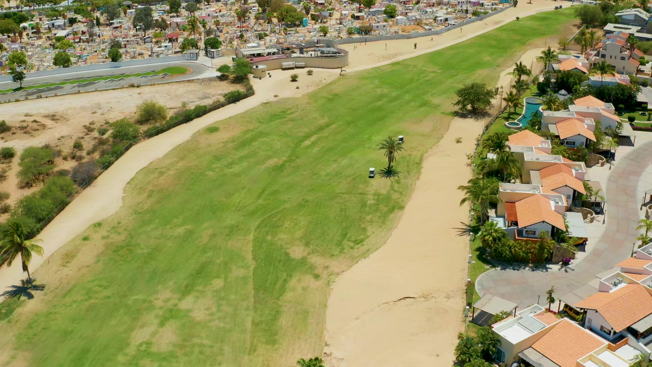 Golf cart on a green fairway near sand and residential houses.