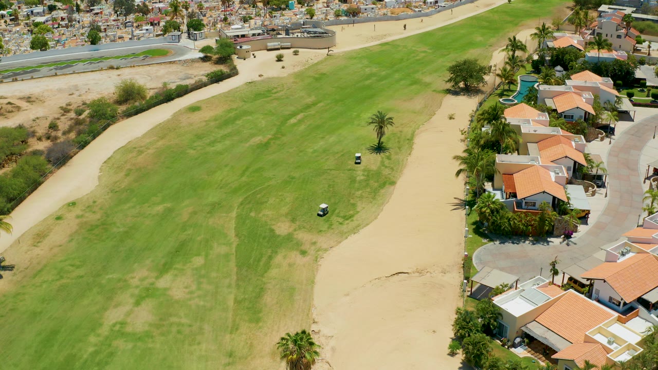 Wide drone view of a golf fairway with a small golf cart near the grass and sand edge.