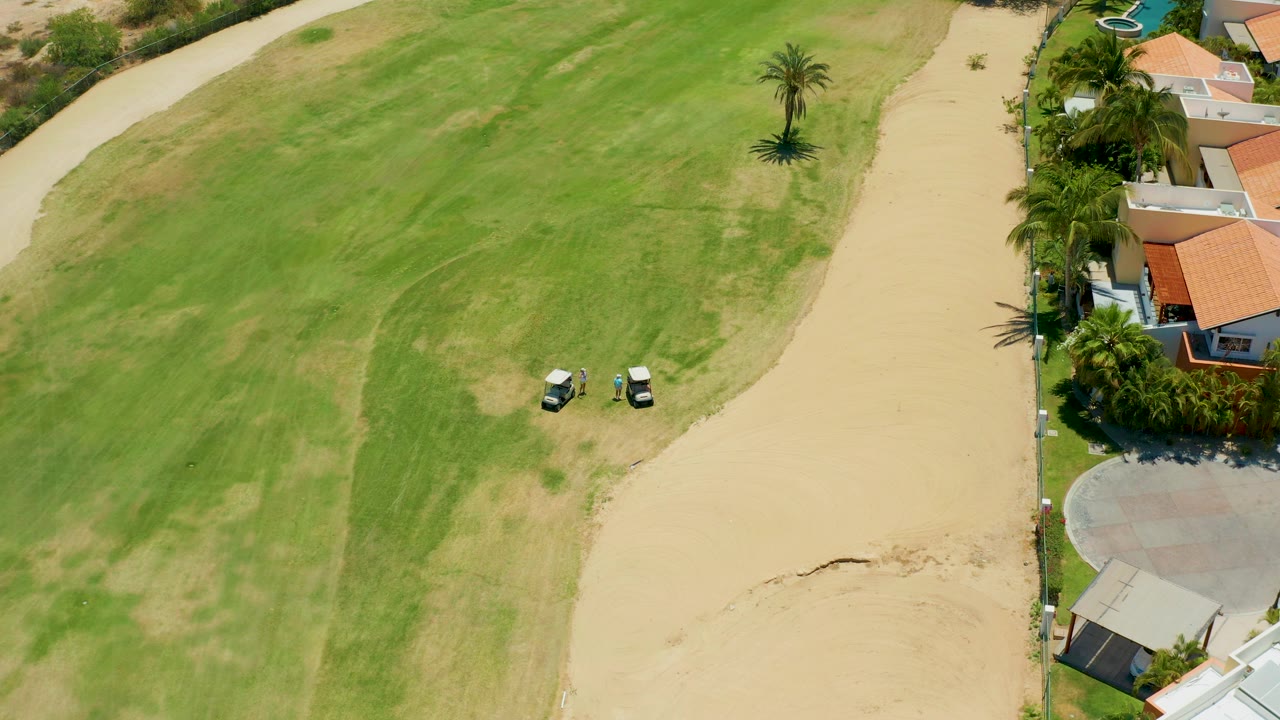Two golf carts on a grassy course beside a sandy path.