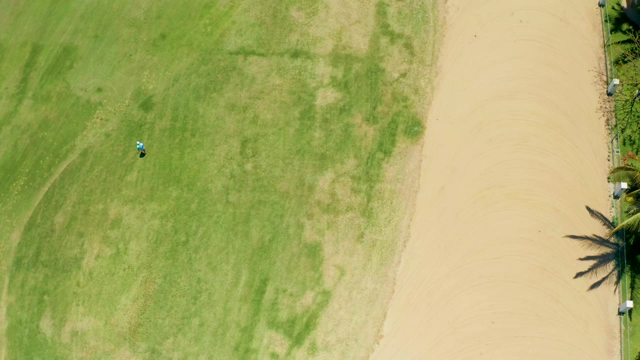 Aerial field view with the sandy path at right and a small vehicle farther down the grass.