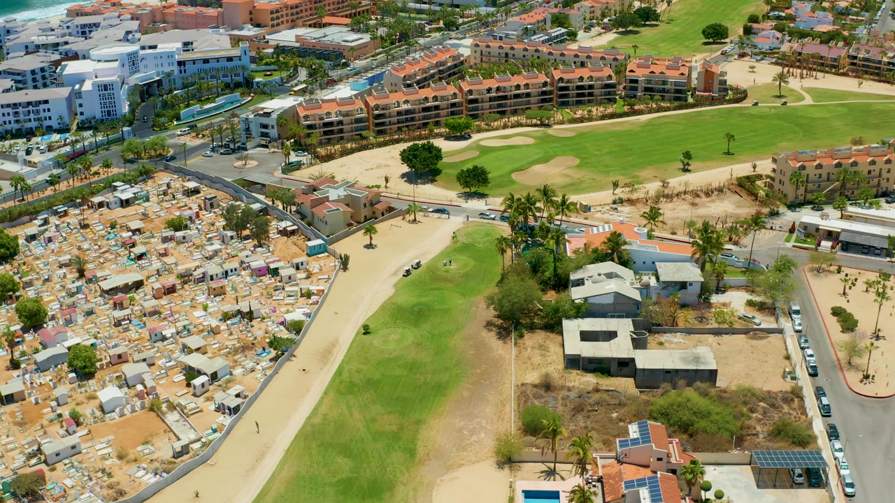 Aerial view of tents beside a green strip, curved roads, palms, and resort-like buildings.
