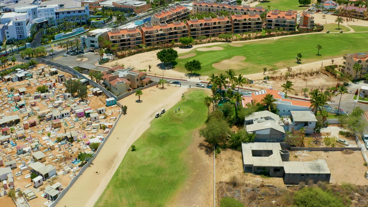 Aerial view of golf grass, sandy path, housing, and resort buildings.