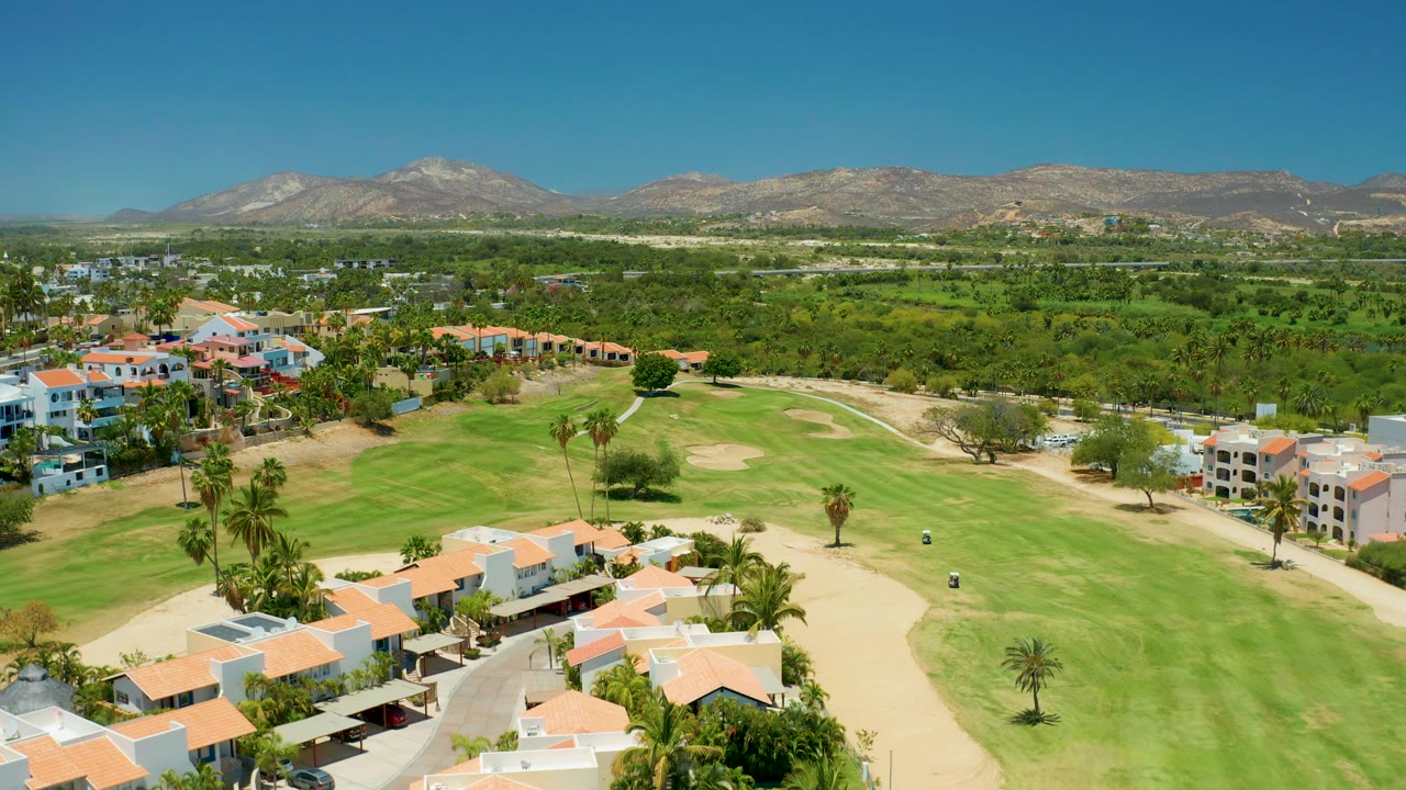 Golf course fairway and sand traps beside red-roofed residential buildings.