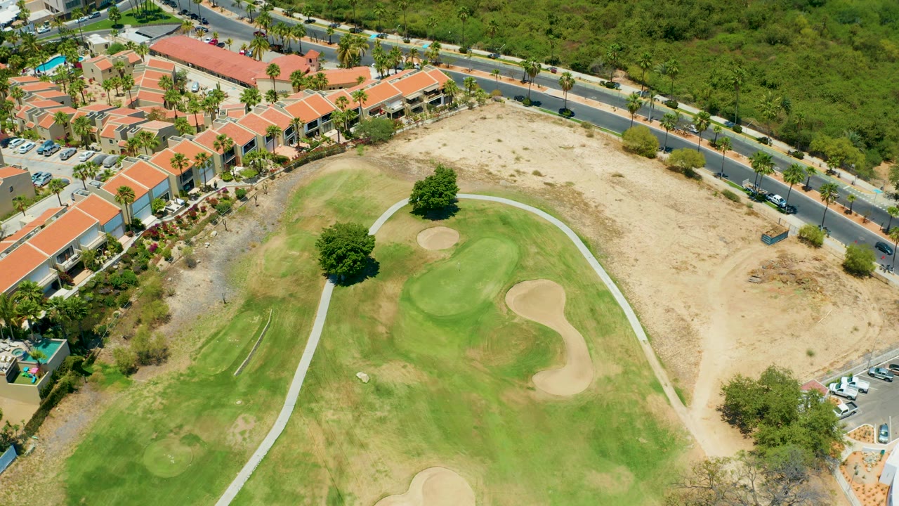 Overhead golf green with sand traps beside a curved road and buildings.