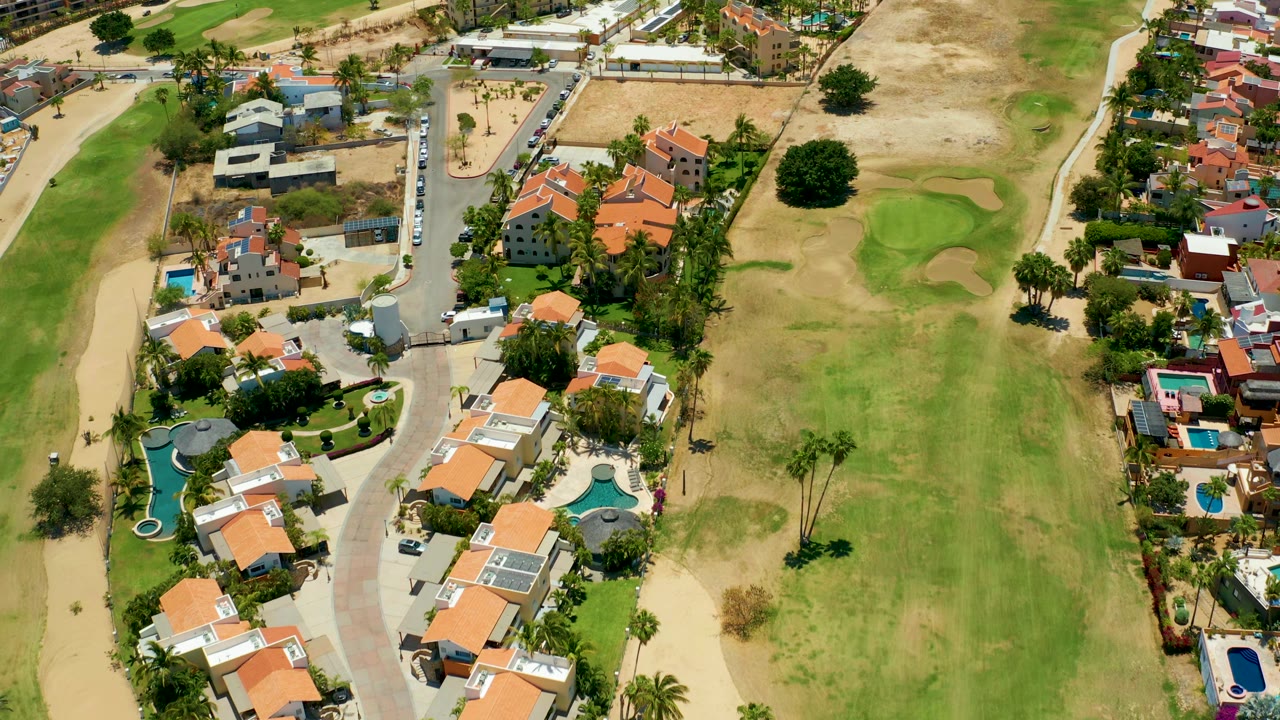 Drone view of villas, pools, road, and golf greens.