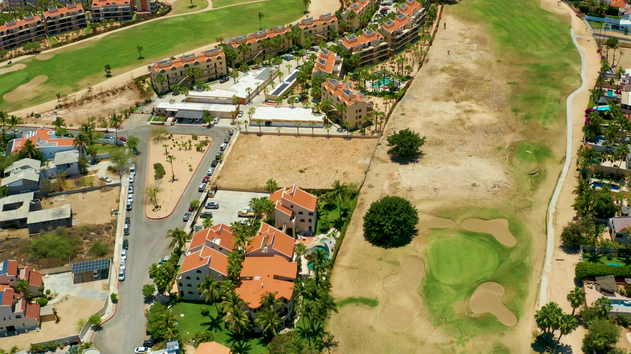 Aerial view of neighborhood buildings next to golf course paths and greens.