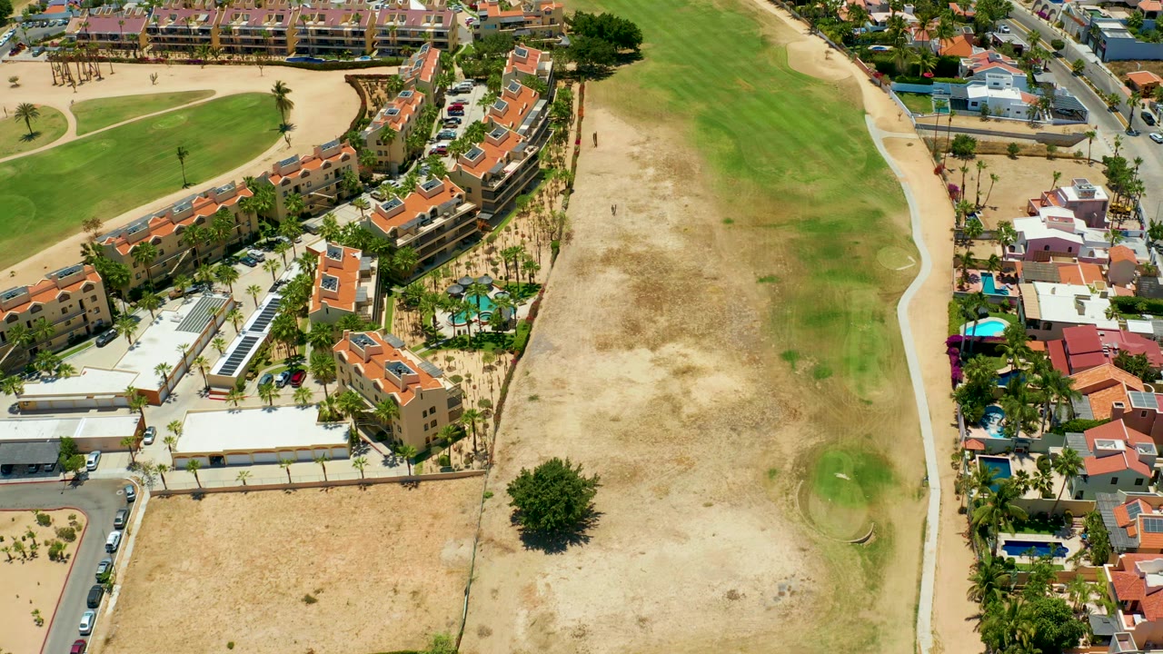 Drone view of residences, road, path, and patchy grass field.
